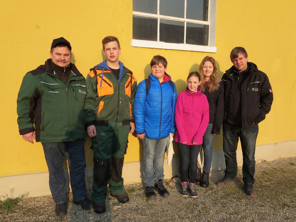 Sechs Personen in bunter Freizeit- und Arbeitskleidung lächeln vor einer gelben Wand in die Kamera.