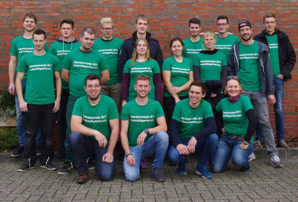 Gruppe lächelnder Menschen in grünen T-Shirts vor Backsteinwand, "Talentschmiede 2017" steht darauf.
