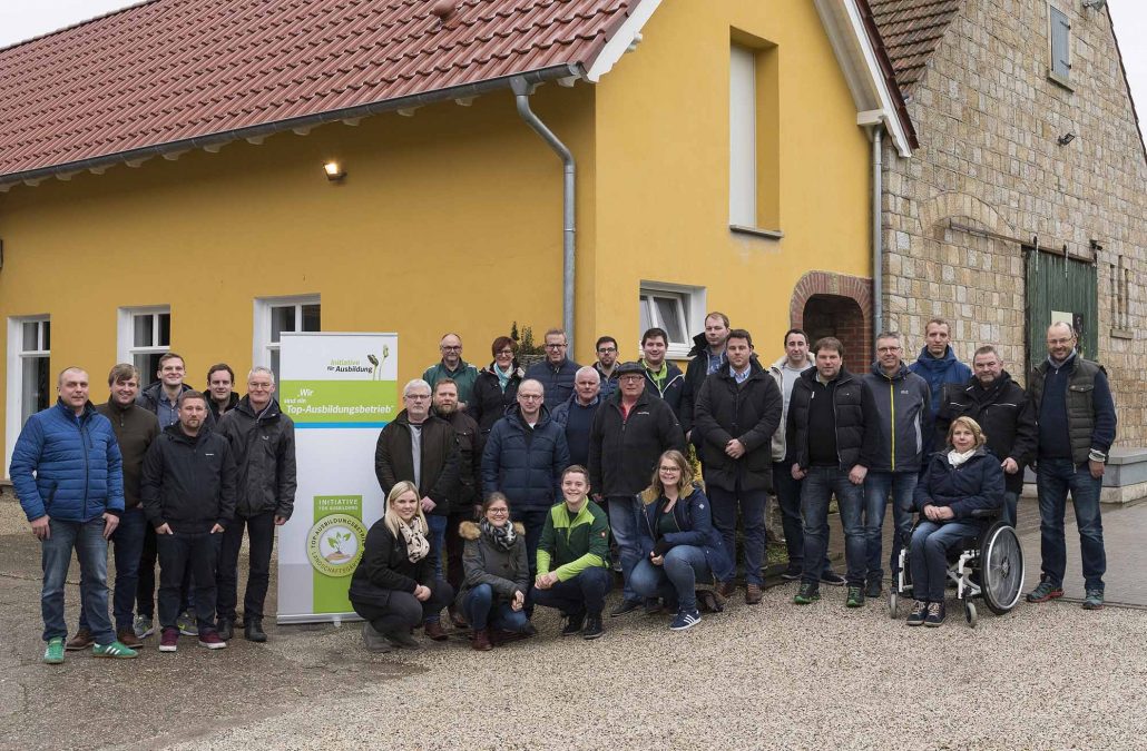 Eine Gruppe von Menschen posiert vor einem gelben Gebäude mit einem Schild „Top-Ausbildungsbetrieb“.