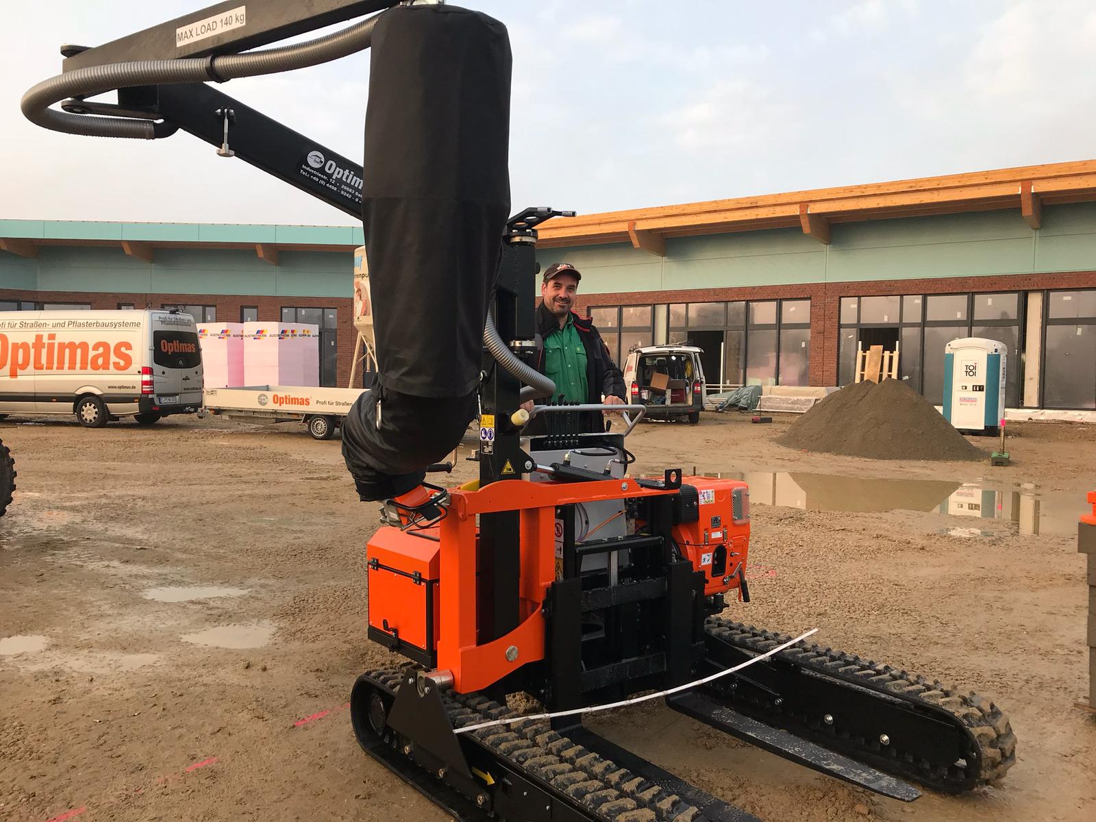 Eine orangefarbene Baumaschine und eine Person auf einer geschäftigen Baustelle mit unfertigem Gebäude.
