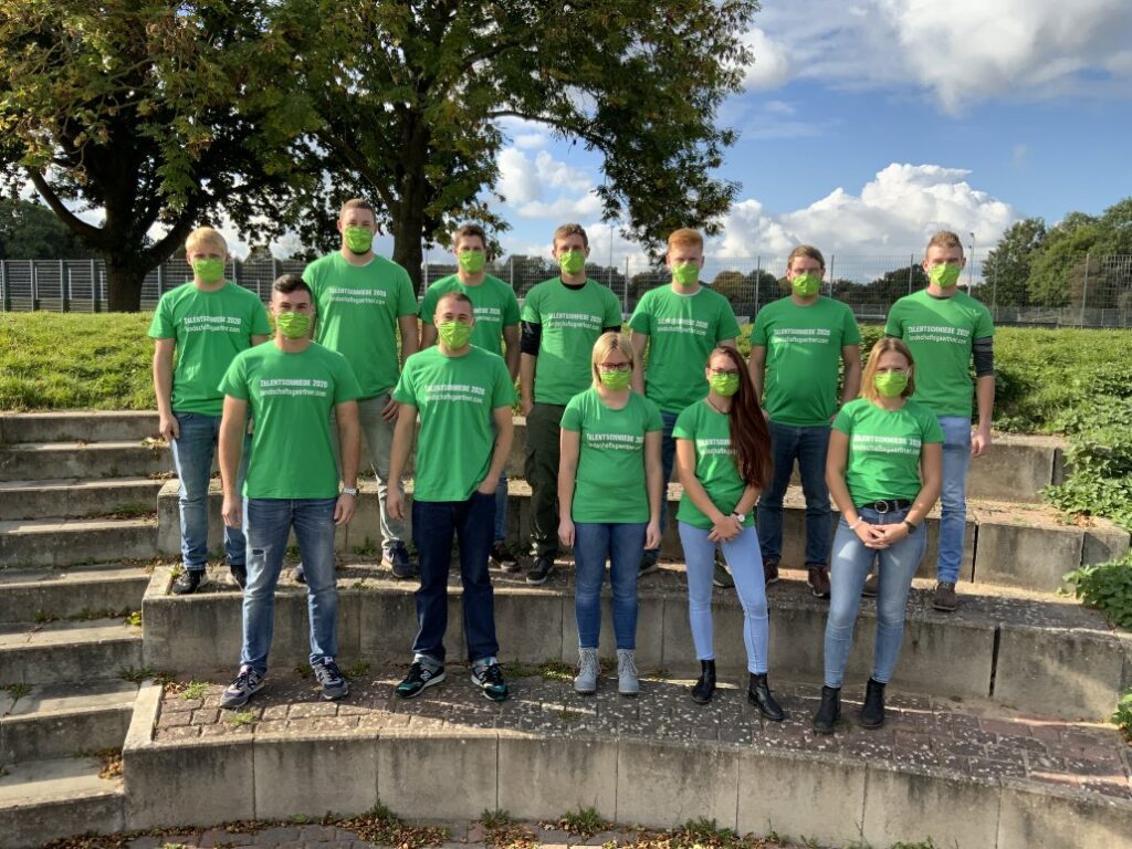 Eine Gruppe von 13 Personen in grünen T-Shirts und Masken posiert auf einer Treppe im Freien.