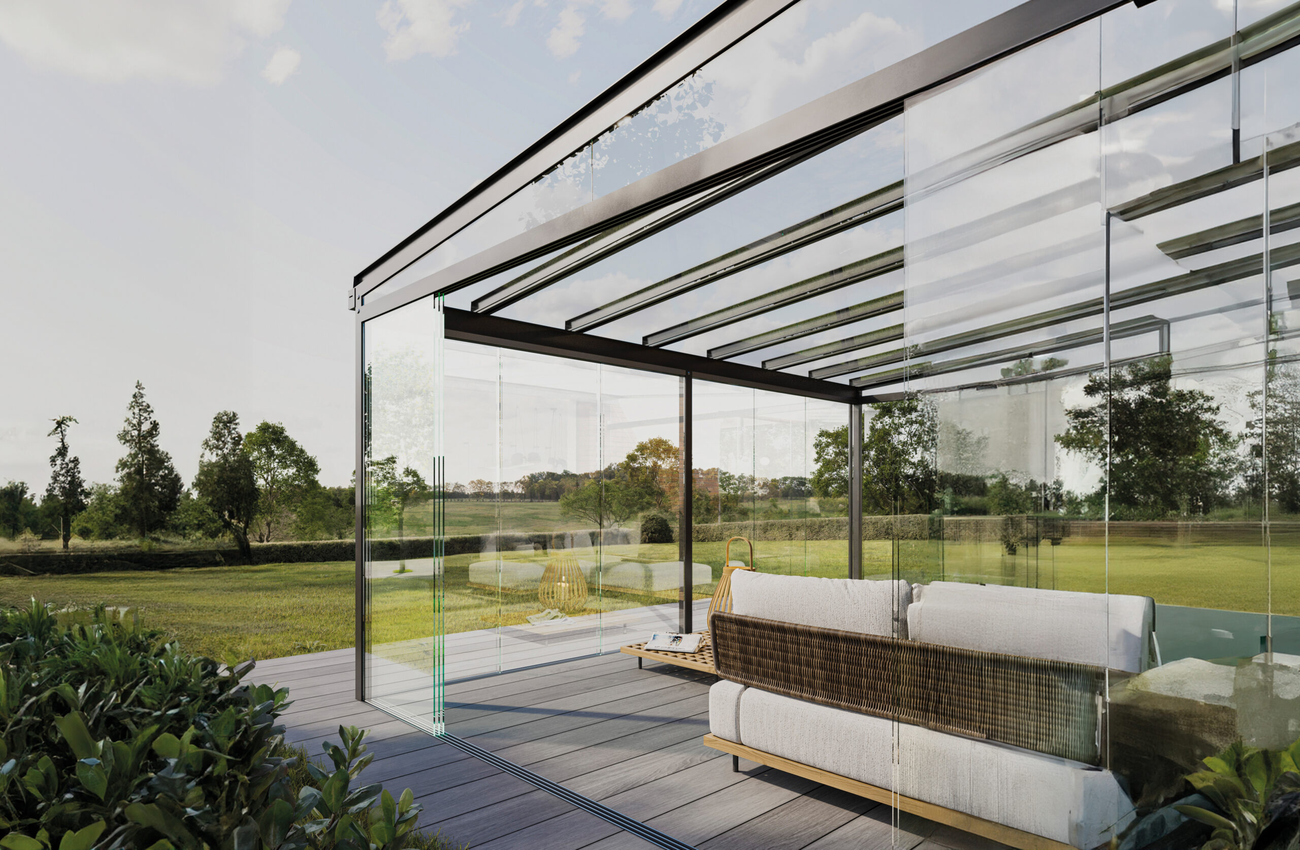 Moderne Terrasse mit Glasüberdachung, Sofa und Couchtisch, umgeben von grüner Landschaft.