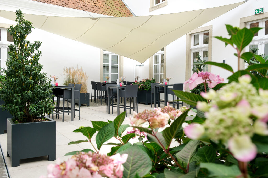 Stilvolle Terrasse mit modernen Möbeln, blühenden Hortensien und einem großen Sonnensegel für Schatten.
