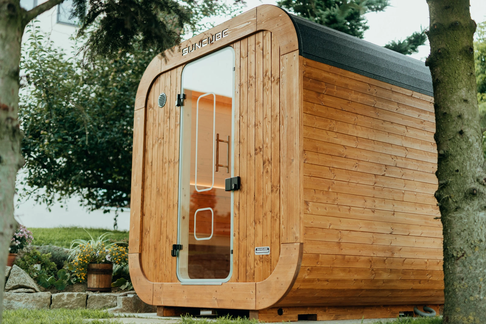 Moderne Holzhütte mit Glastür in natürlicher Umgebung, umgeben von Grünpflanzen und Bäumen.