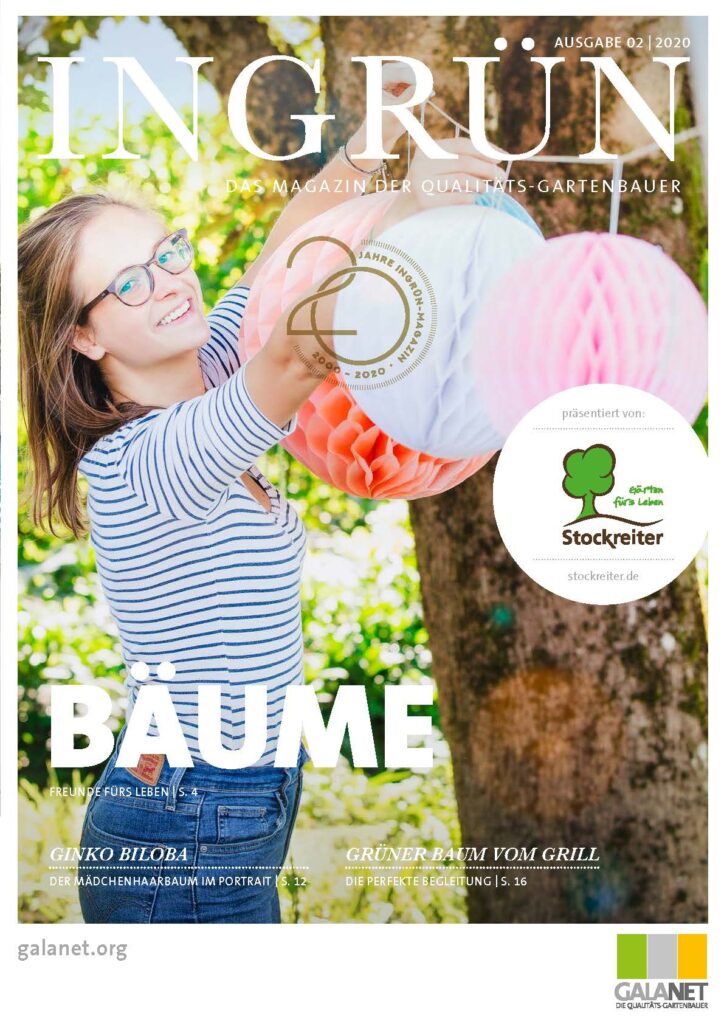 Eine Person hängt bunte Papierdekorationen in einem Garten auf, umgeben von einem Baum und fröhlichen Farben.