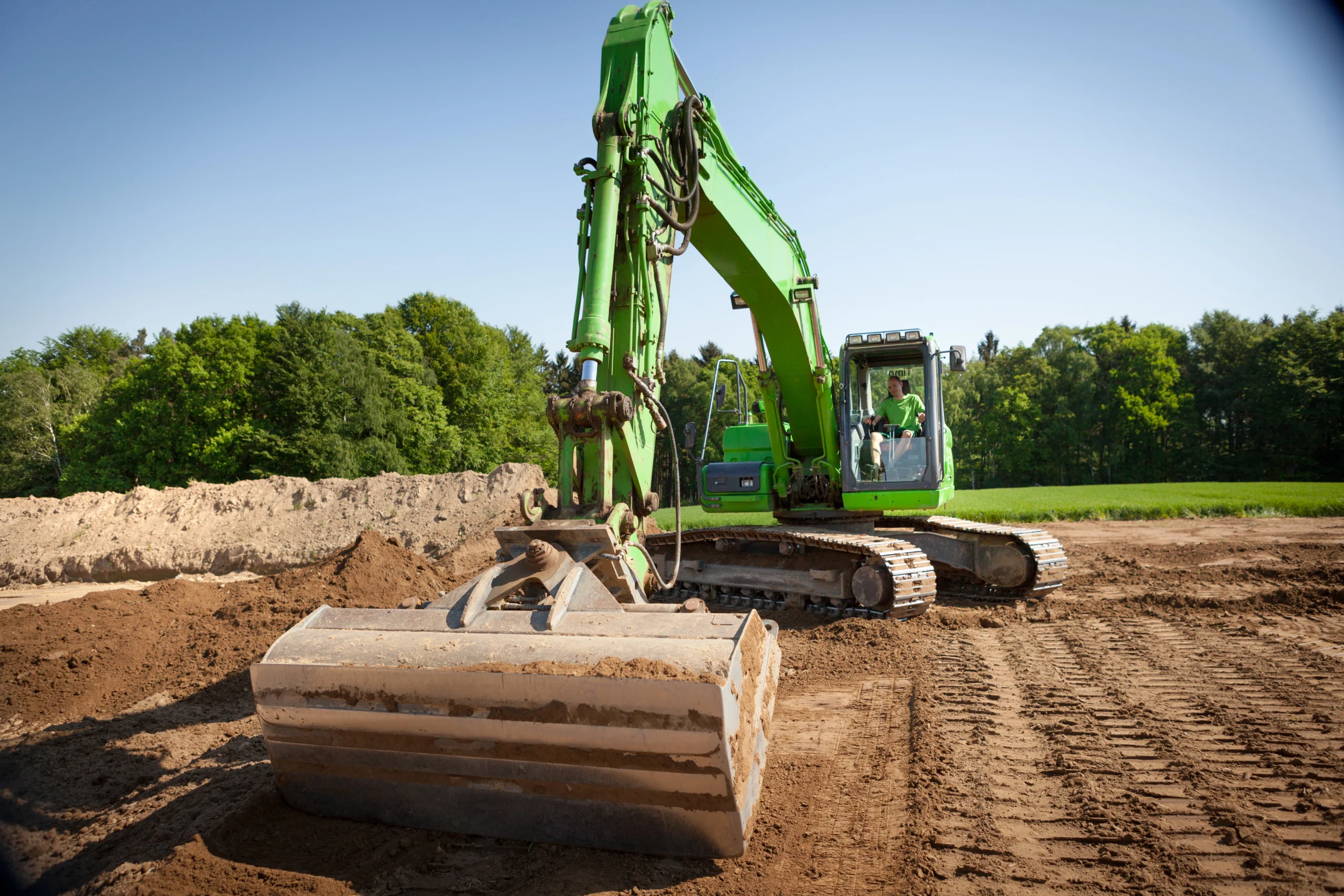 Ein großer grüner Bagger steht still auf einer Baustelle, mit einer Schaufel auf dem Boden.