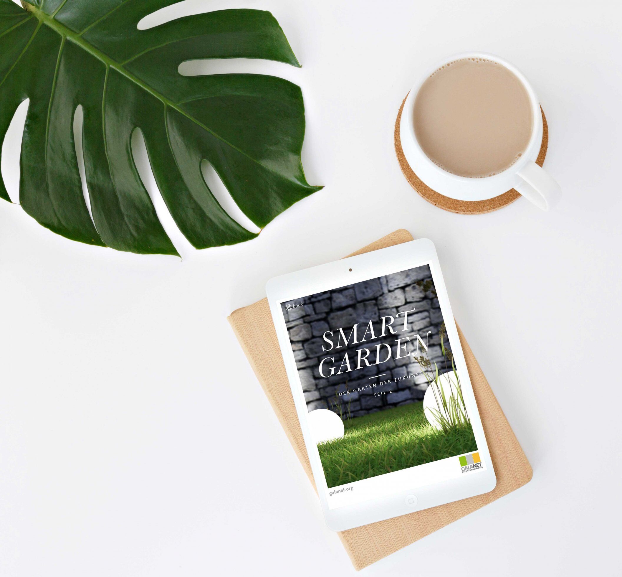 Ein Tablet mit "SMART GARDEN"-Cover, umgeben von einem Notizbuch, einer Kaffeetasse und einem Monstera-Blatt.