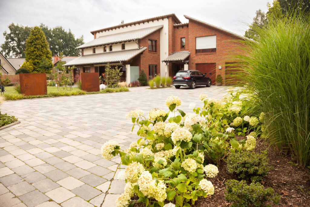 Modernes zweistöckiges Backsteinhaus mit gepflegtem Garten und geparktem Auto auf gepflastertem Hof.