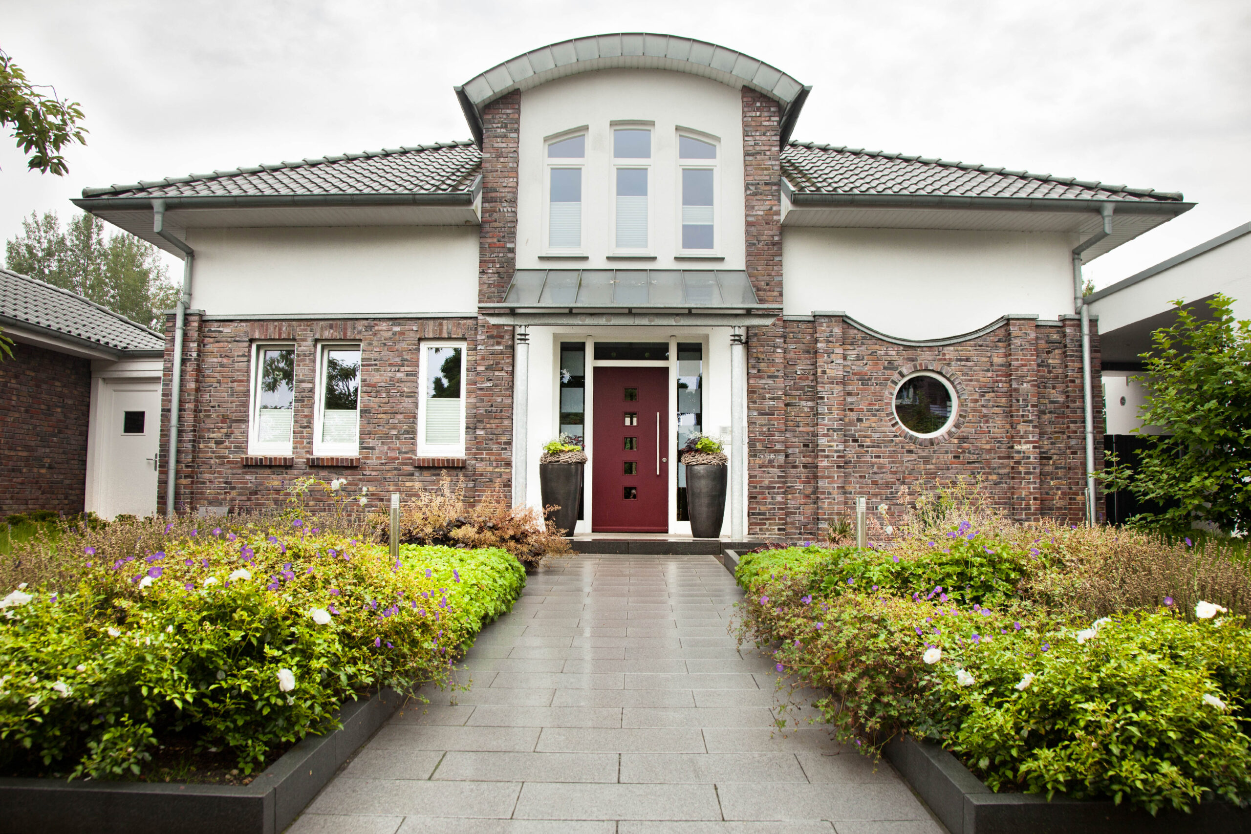 Modernes Haus mit Backsteinfassade, roter Tür und gepflegtem Garten in ruhiger Wohngegend.