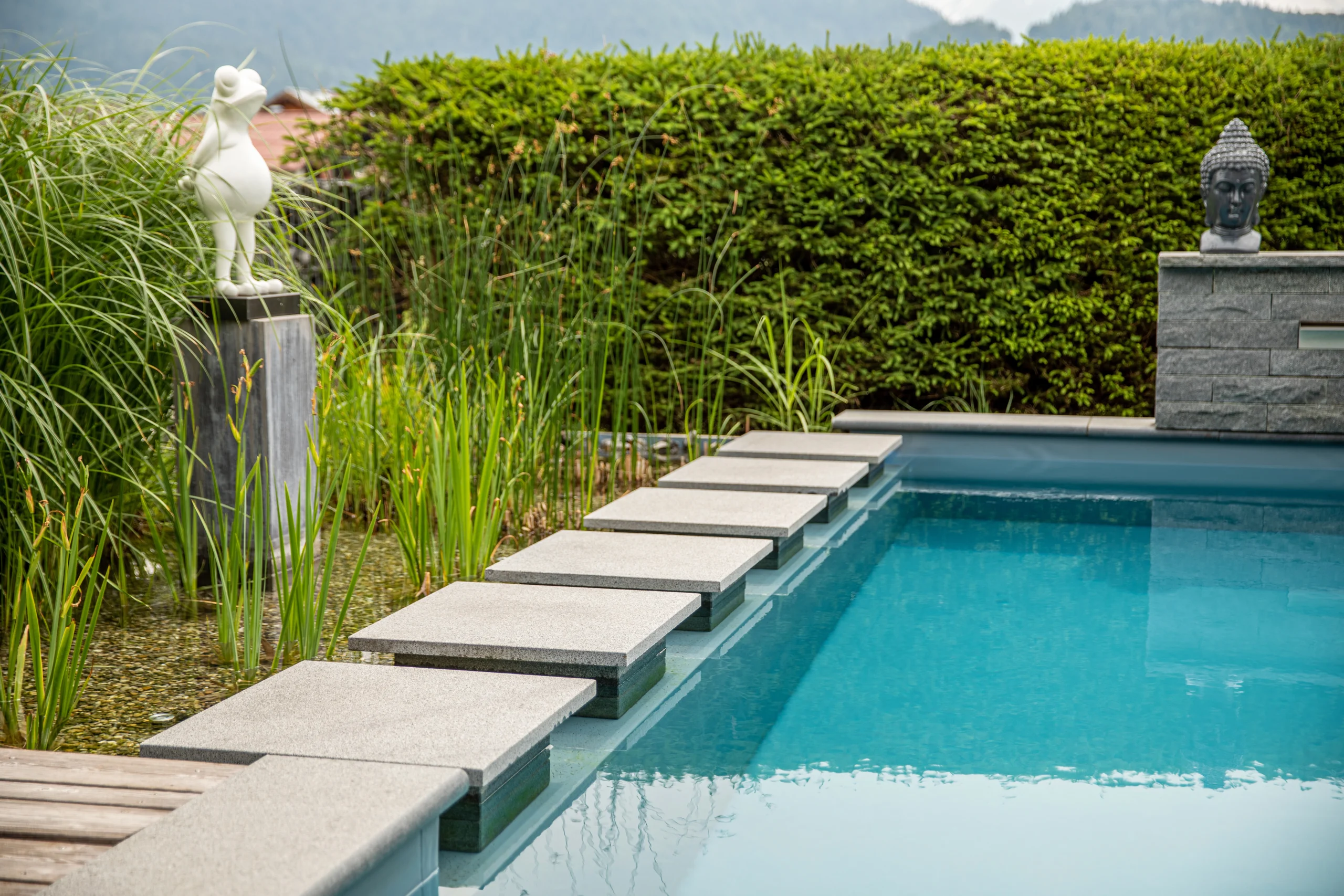 Ein moderner Garten mit rechteckigem Pool, Steinplattenweg, umgeben von Pflanzen und Skulpturen.