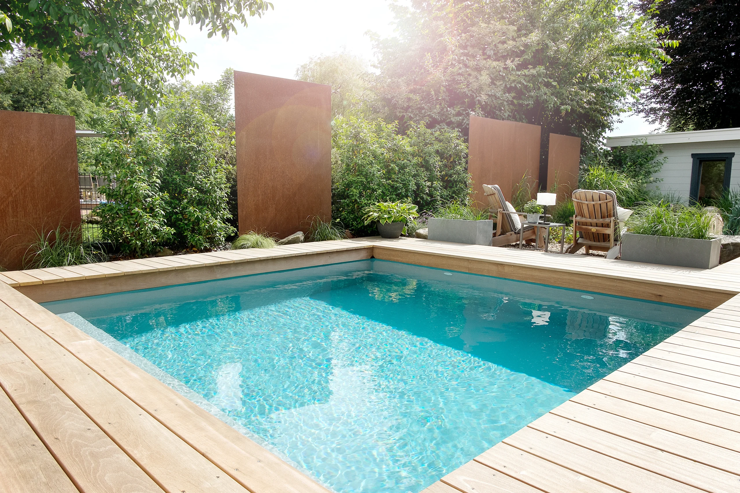 Moderner Außenbereich mit Pool, Holzdeck, Sitzbereich und üppigen Pflanzen, umgeben von Metallplatten.