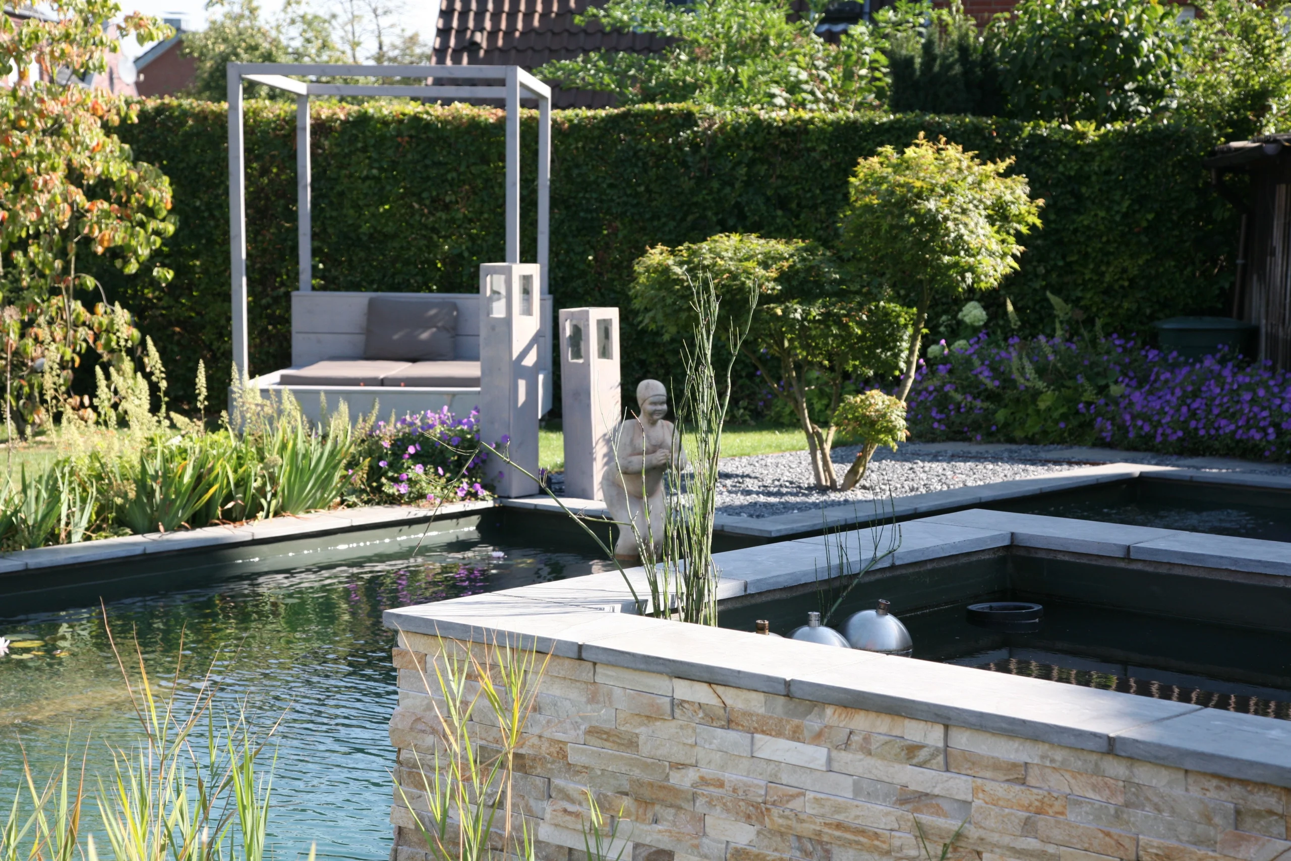 Moderner Garten mit rechteckigem Teich, Buddha-Statue, kubischer Sitzgelegenheit und grüner Bepflanzung.