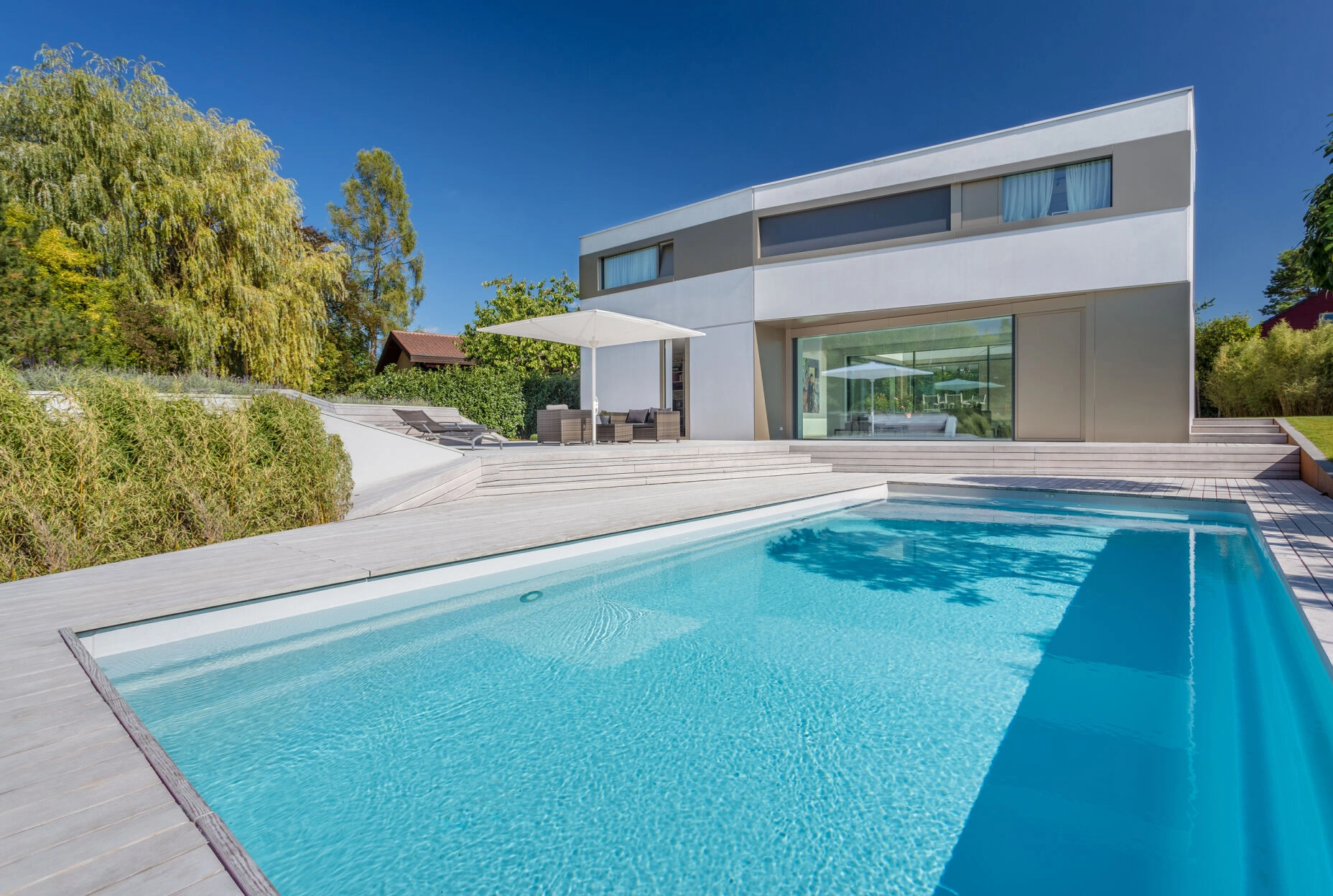 Modernes zweistöckiges Haus mit großem Pool, Terrasse und Garten; ruhige, luxuriöse Atmosphäre.