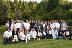 Eine große Gruppe von Menschen posiert im Park, einige halten stolz Zertifikate in die Kamera.