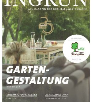 Ein Holztisch im Garten mit Gläsern, Karaffen und Blumen, umgeben von unscharfen Pflanzen im Hintergrund.