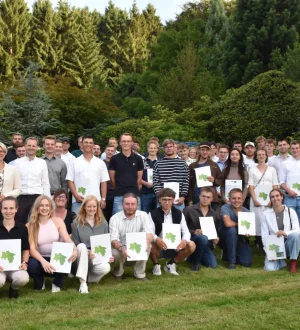 Eine große Gruppe von Menschen posiert im Park, einige halten stolz Zertifikate in die Kamera.