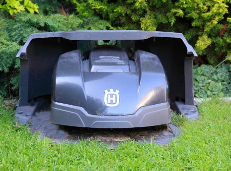 Ein automatischer Rasenmäher in dunklem Grau steht in seiner Ladestation, umgeben von grünem Gras.
