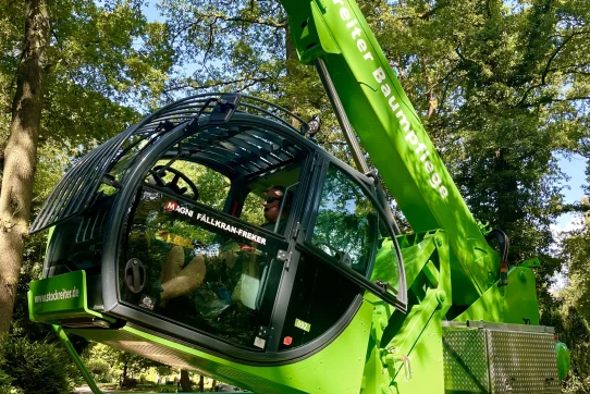 Ein leuchtend grüner Kran von „Stockreiter Baumpflege“ arbeitet konzentriert in einer bewaldeten Umgebung.