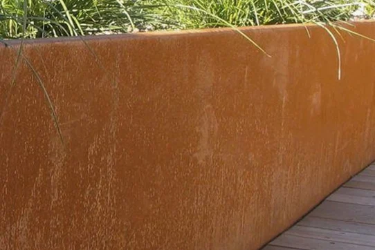 Rostfarbener Cortenstahl-Pflanzkübel mit grünen Pflanzen auf Holzterrasse, kontrastreich und modern.