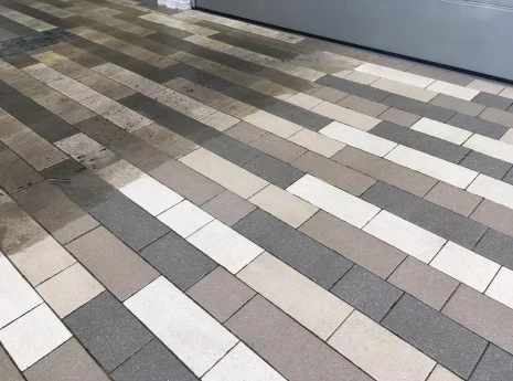 Gepflasterter Boden aus rechteckigen Steinen in Grautönen, Beige und Weiß, mit regelmäßigen Fugen.