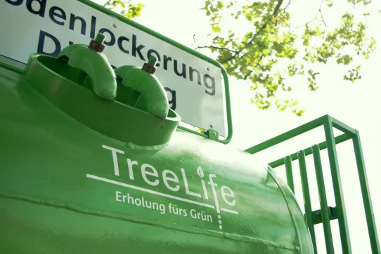 Grünes Gerät mit "TreeLife"-Logo, umgeben von Natur, zur Pflege von Pflanzen und Bodenlockerung.