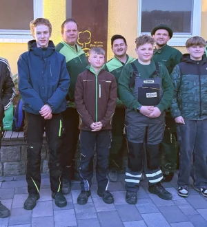 Elf Personen in Outdoor-Kleidung posieren vor einer gelben Wand für ein Gruppenfoto.